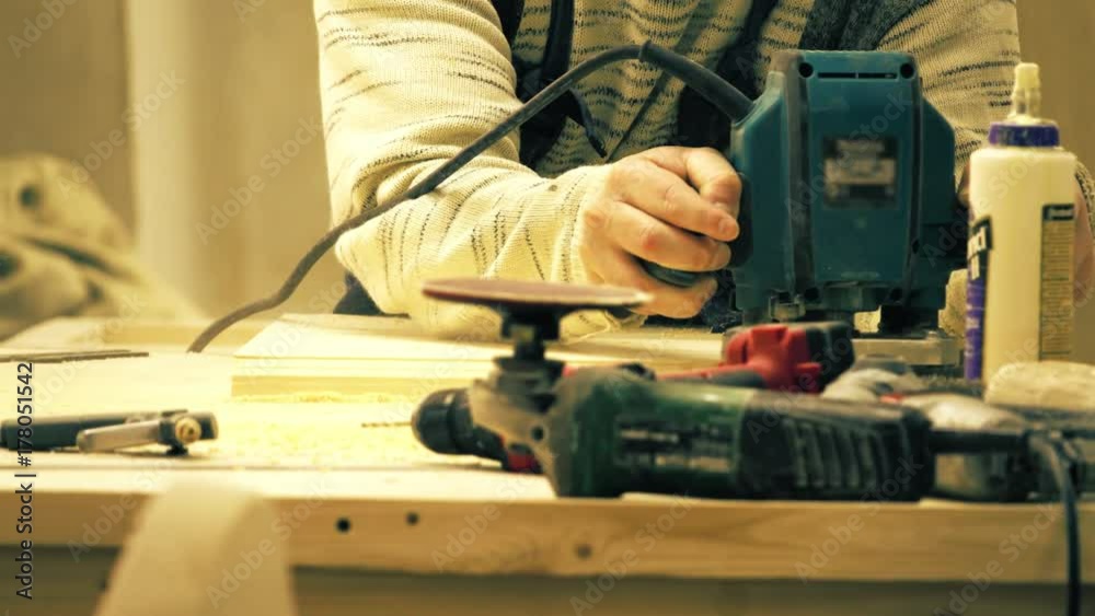 Unknown carpenter sawing wooden board with a portable jigsaw in a carpentry workshop Unknown carpenter sawing wooden board with a portable jigsaw in a carpentry workshop