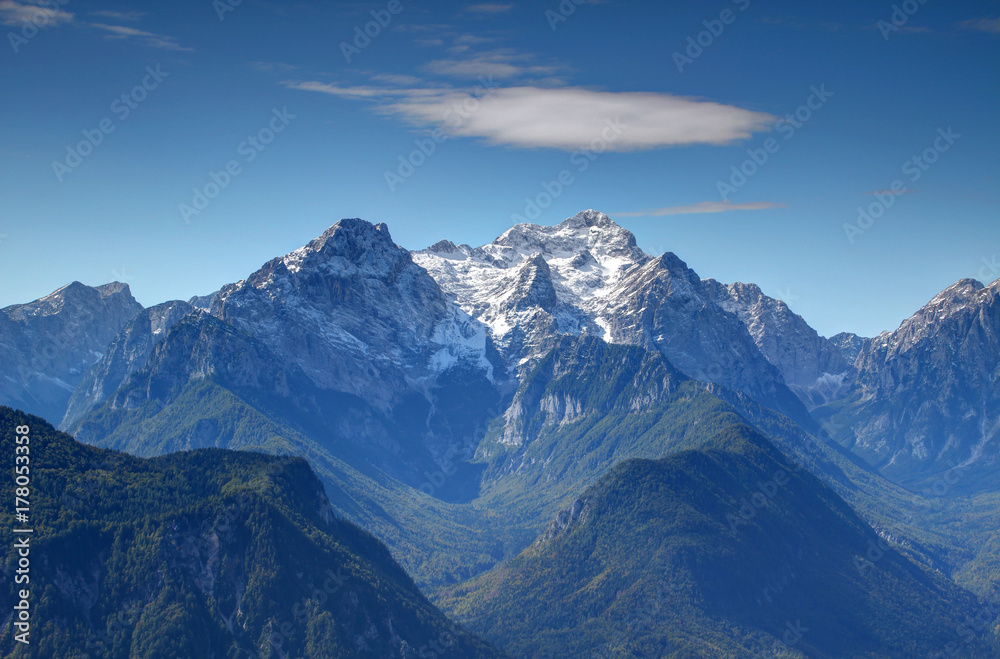 Snowy Triglav peak, highest point of Slovenia, from the north with sharp Rjavina peak and green forests of deep Vrata and Kot Valley against the blue sky, Triglav National Park, Julian Alps, Europe