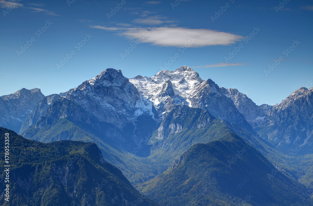 Snowy Triglav peak, highest point of Slovenia, from the north with sharp Rjavina peak and green forests of deep Vrata and Kot Valley against the blue sky, Triglav National Park, Julian Alps, Europe Snowy Triglav peak, highest point of Slovenia, from the north with sharp Rjavina peak and green forests of deep Vrata and Kot Valley against the blue sky, Triglav National Park, Julian Alps, Europe