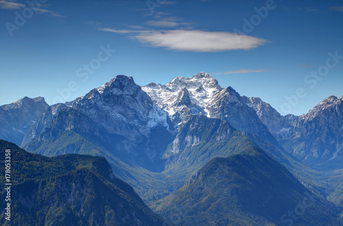 Snowy Triglav peak  highest point of Slovenia  from the north with sharp Rjavina peak and green forests of deep Vrata and Kot Valley against the blue sky  Triglav National Park  Julian Alps  Europe