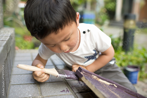 Happy boy focusing on brushing deep purple paint on board in garden photo