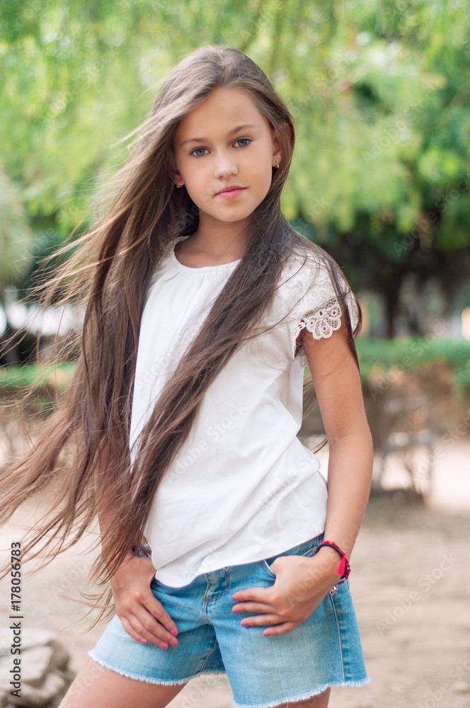 Beautiful school girl with long hair in the park.  Prety Girl with a model appearance and with fashionable poses. Child of 8 years.