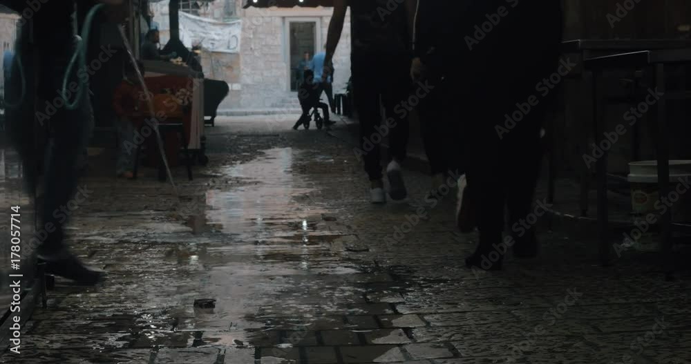 ACRE, ISRAEL- MARCH 12, 2017: Narrow street with ice-cream vendor and people passing by. Man washing the ground with a hose ACRE, ISRAEL- MARCH 12, 2017: Narrow street with ice-cream vendor and people passing by. Man washing the ground with a hose