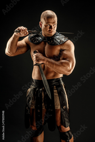 Severe barbarian in leather costume with two swords. Portrait of balded muscular gladiator. Studio shot. Black background. photo