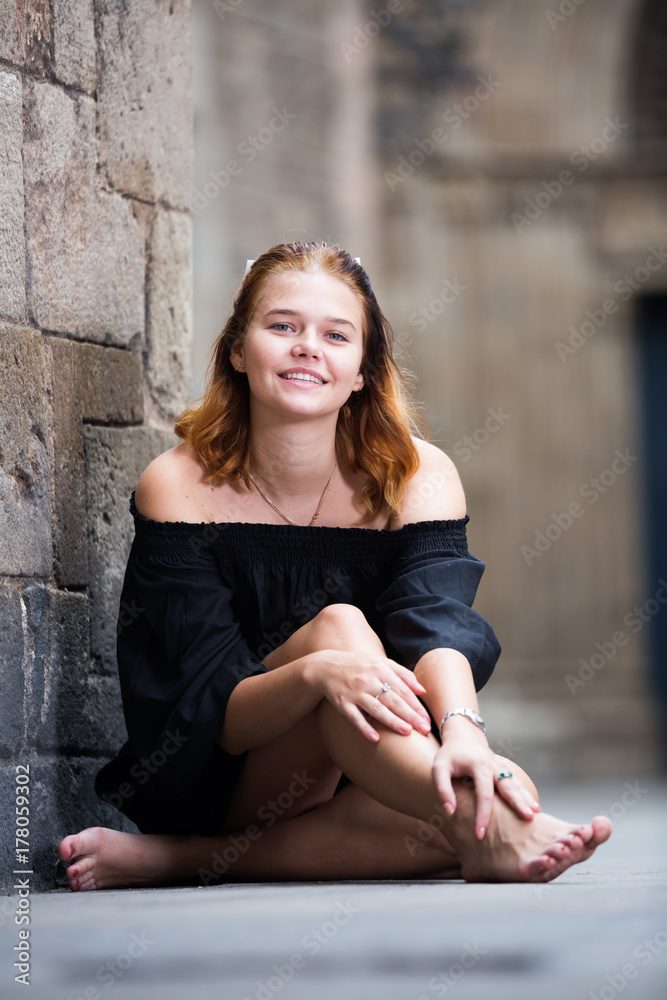 Cheerful girl sitting barefoot near the brick wall