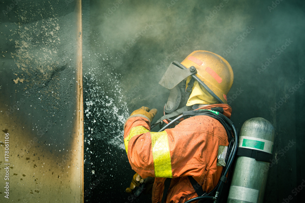 Obraz premium a firefighter water spray by high pressure nozzle to fire surround by smoke copy space