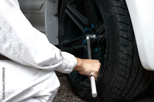 Hands of mechanic in white uniform holding wrench at the repair garage background. Car service concept.