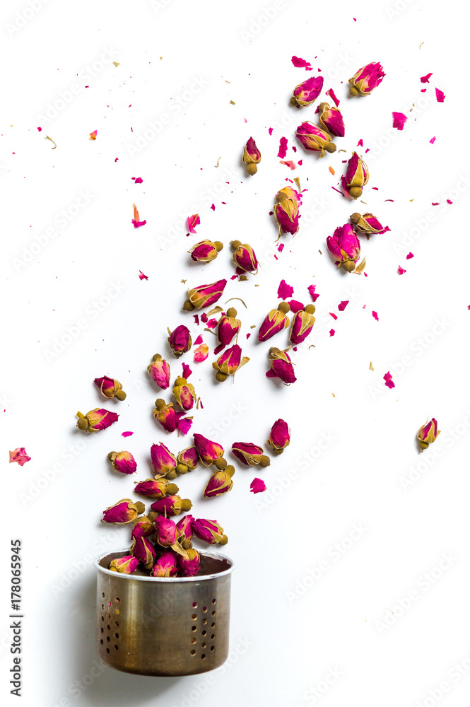 Obraz premium Rose tea flowers flying out of kettle colander on white