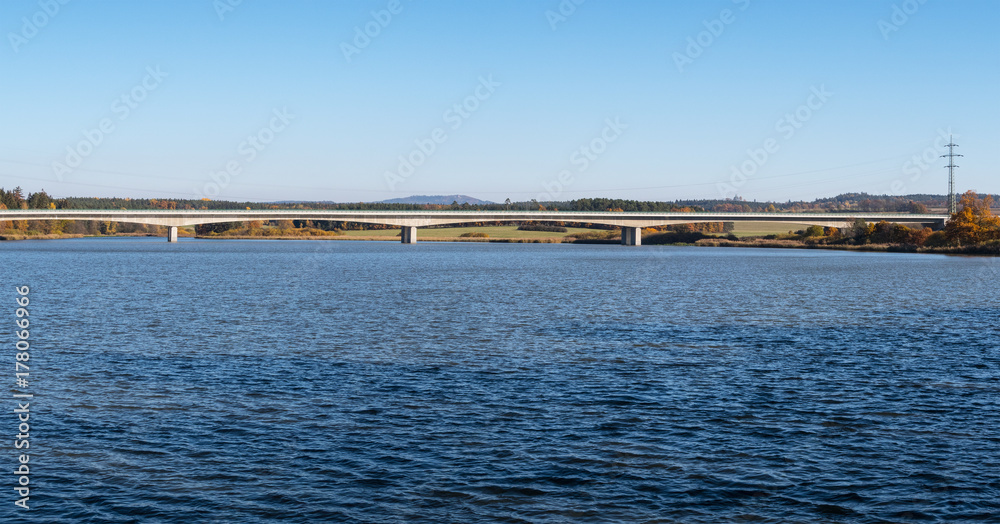 Beautiful view of the motorway bridge over a water. Landscape with rippled pond in the foreground, the concrete bridge and a forest on the horizon.