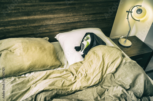 Fotografie Grunge Halloween scary scene/Zombie entity tucked in the bed with open mouth and black hood waiting to scare someone as a prank