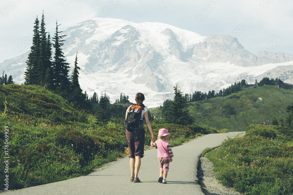 Mother and young daughter holding hands and walking on trail, Mt. Rainier in distance Mother and young daughter holding hands and walking on trail, Mt. Rainier in distance