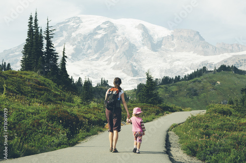 Mother and young daughter holding hands and walking on trail, Mt. Rainier in distance photo