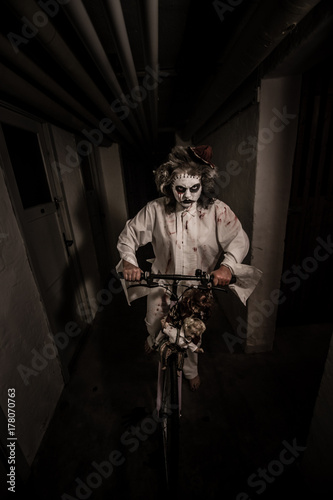 Night ride with dolls.Creepy clown girl riding a bicycle with dolls in a scary room photo