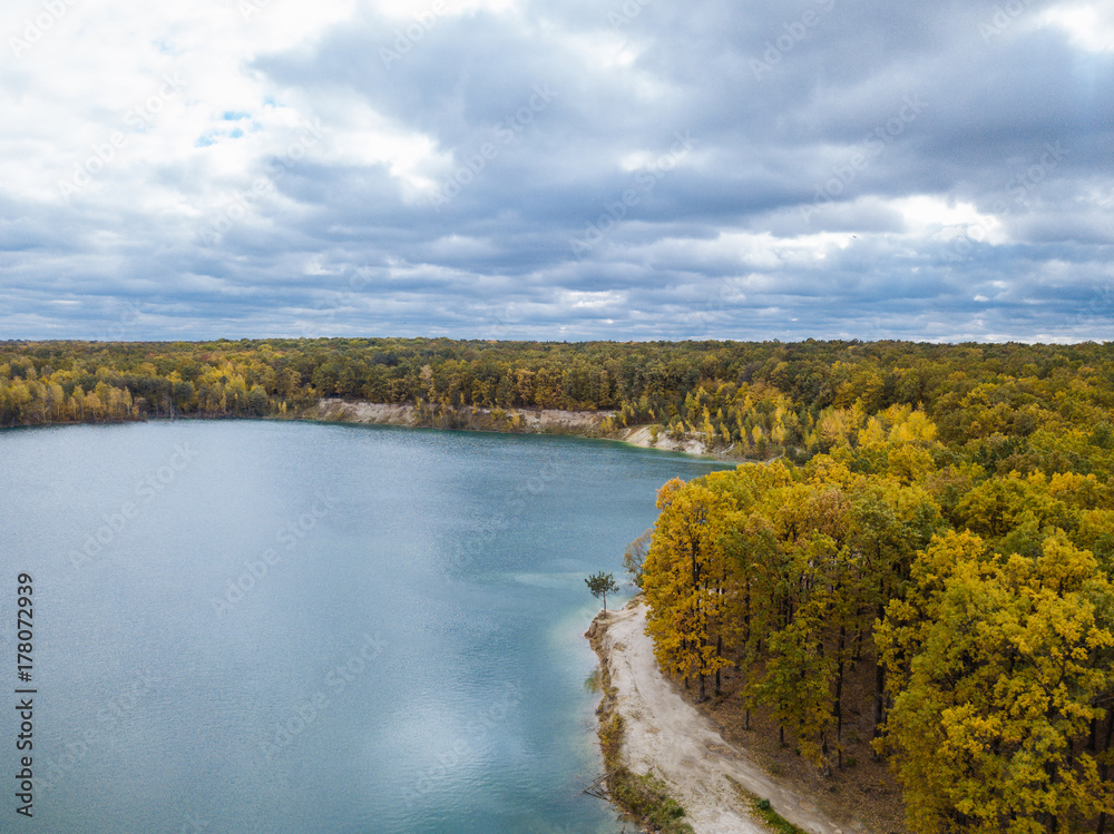 Aerial view of a beautiful autumn landscape with a river surrounded by forest, with a dramatic sky.