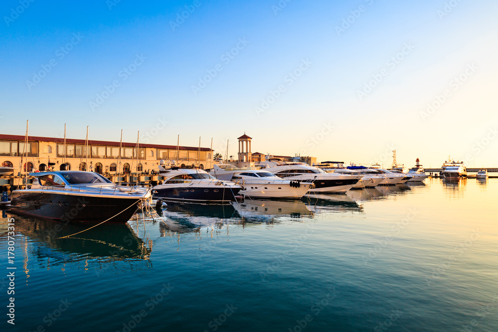 Luxury yachts and motor boats in sea port at sunset.