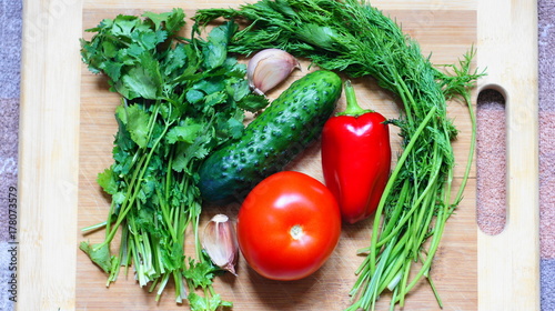 Still life with vegetables. A set of vegetables consisting of tomato, cucumber, bell pepper, parsley, dill and garlic. This is on the cutting board and is about to turn into a salad.