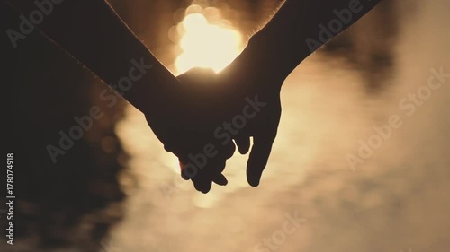 Close up of two Lovers Joining Hands. SLOW MOTION 240 fps. Detail Silhouette of Man and Woman holding hands over the Sunset Lake Background. Couple Trust, Love and Happiness concept. 
