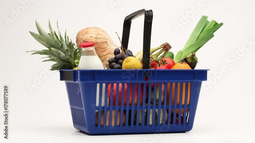 Supermarket shopping basket filled with groceries moving on white background.
