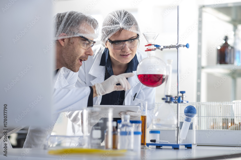 Two scientists working in lab together looking at flask Two scientists working in lab together looking at flask