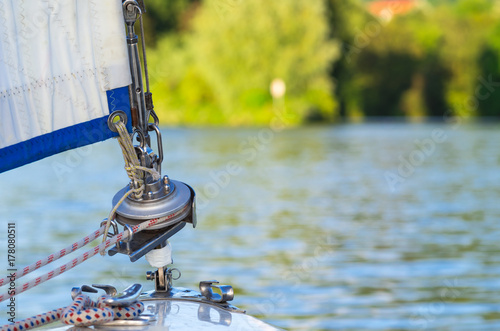 Bow of a sailing yacht with a part of sail, block and sheets on the defocused lake background with copyspace photo