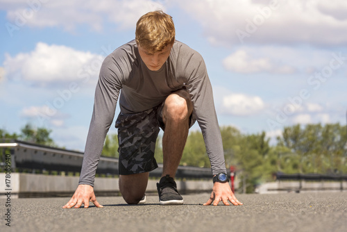 Young man starting run, outdoor in sunny day in sportywear in gray color.