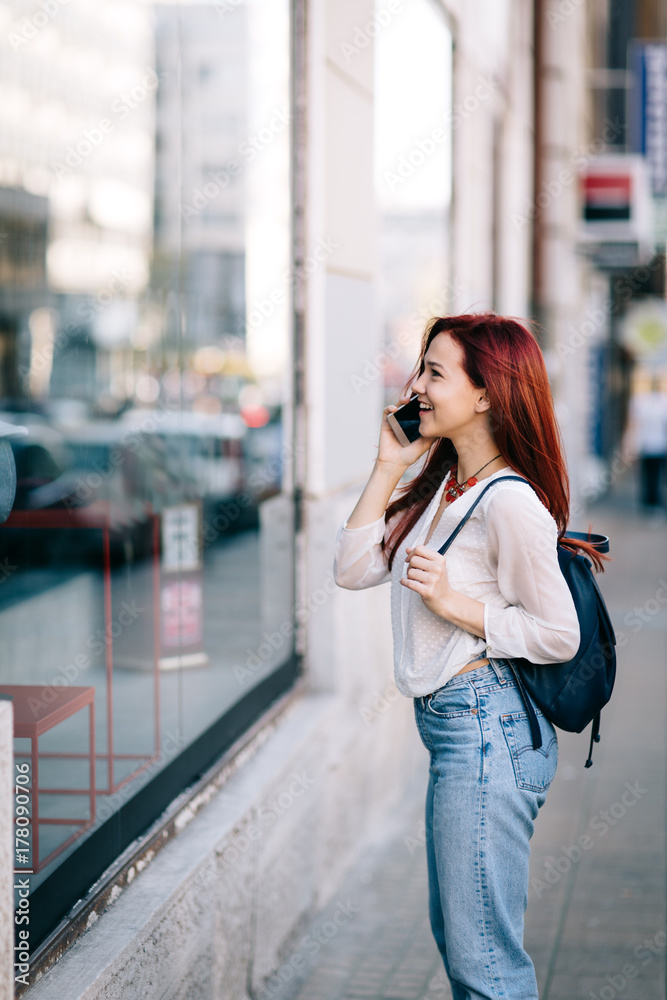 Young woman with coffee to go standing at the street and talking on mobile phone