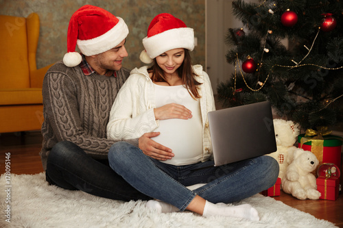 Cheerful young couple in christmas hats sitting on a floor