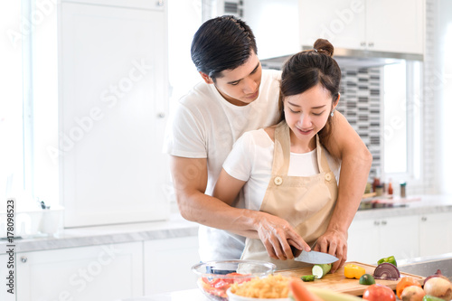 Couple cooking food in kitchen room, Young Asian man and woman together cutting slice vegetables making each salad for dinner menu with fruits at home romantic indoor sweet lover, copy space the left.