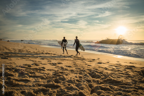 enthusiastic surfers going for surf session in scenic beautiful sunset seascape in capbreton, france
