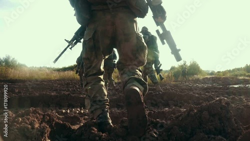 Military soldiers with weapon walking on dirty road