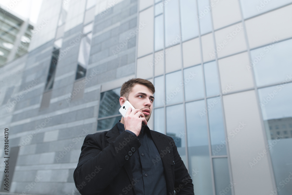 Portrait of a serious young businessman with a beard who speaks by phone on the background of modern ariculture. Business portrait. Portrait of a serious young businessman with a beard who speaks by phone on the background of modern ariculture. Business portrait.