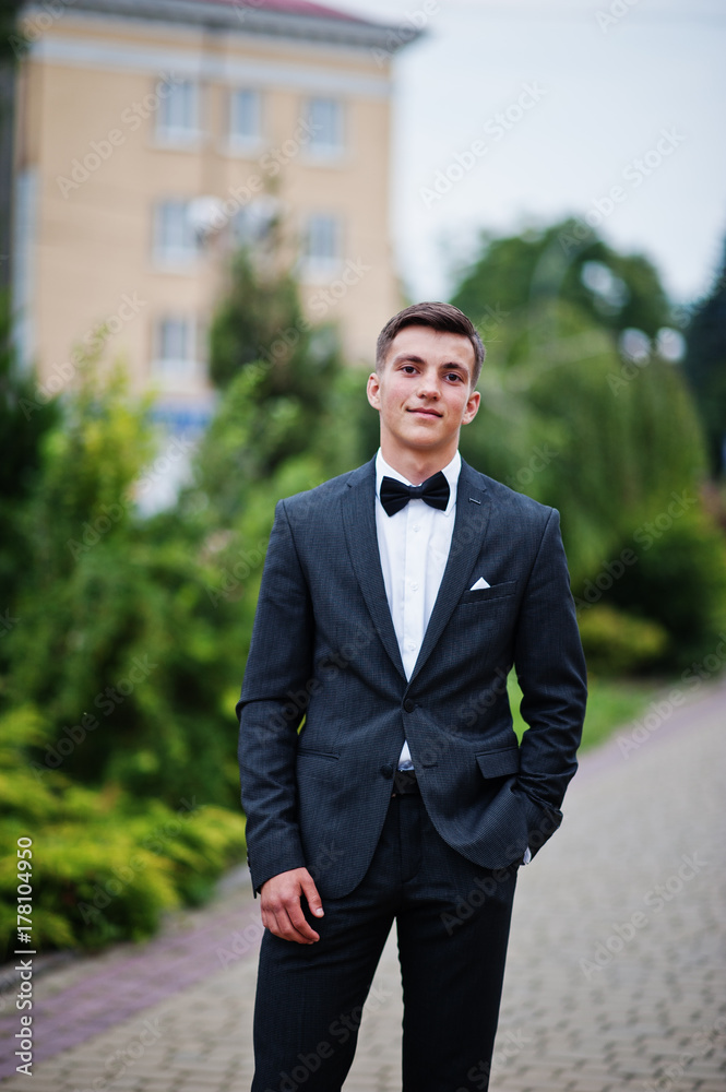 Portrait of a handsome young man in formal fancy suit posing on the pavement in the park on a prom day.