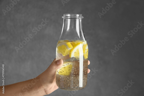 Hand holding bottle of water with chia seeds and lemon on grey background