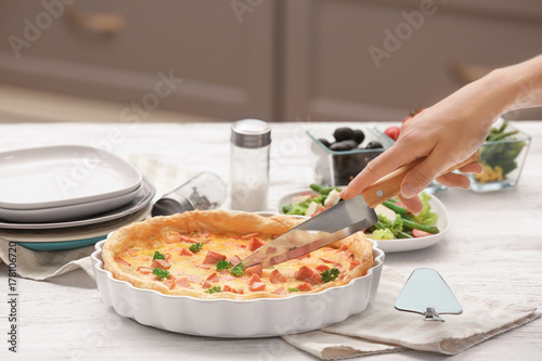 Woman cutting tasty casserole with sausages in baking dish on table