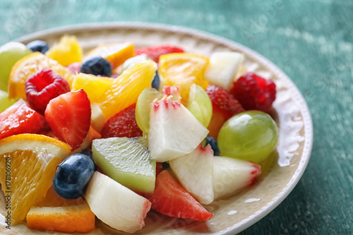 Plate with delicious fruit salad on wooden background