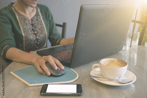 freelance business woman using computer notebook with smartphone and cup of coffee at table in cafe.