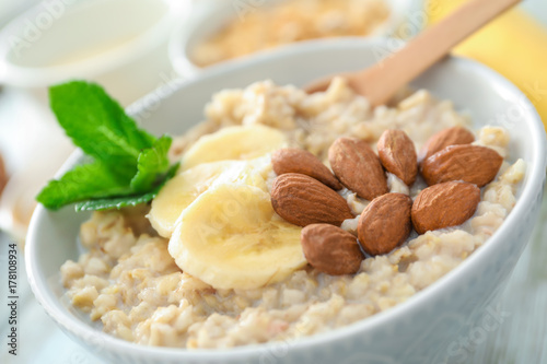Tasty oatmeal with almonds and banana in bowl on table, close up