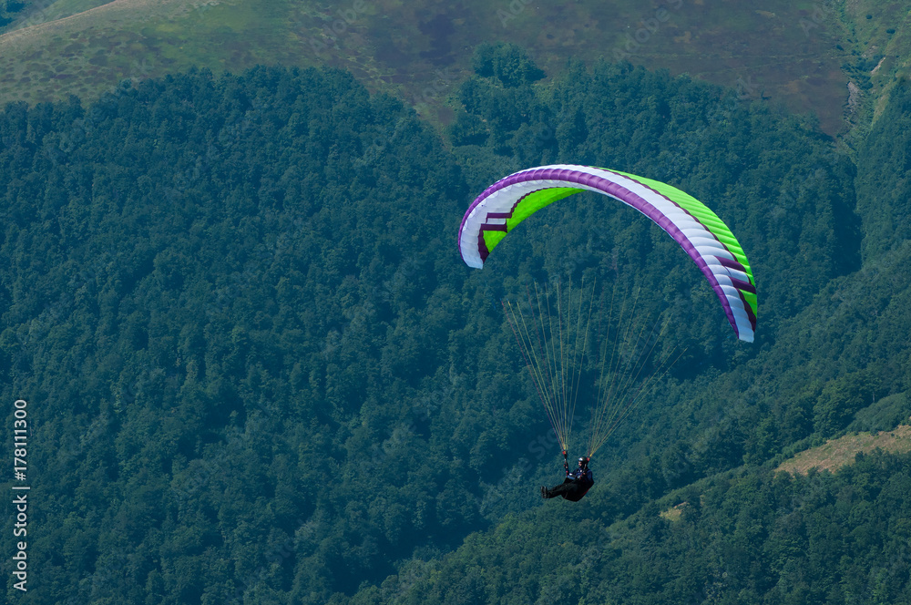 A paraglider flies over a mountain valley on a sunny summer day. Paragliding in the Carpathians in the summer. A paraglider flies over a mountain valley on a sunny summer day. Paragliding in the Carpathians in the summer.