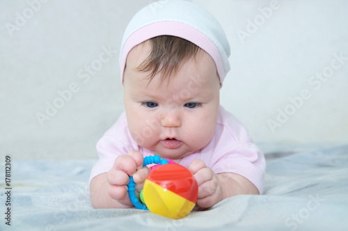 Early brain development. concentrated little baby girl  playing with rattle lying on bed