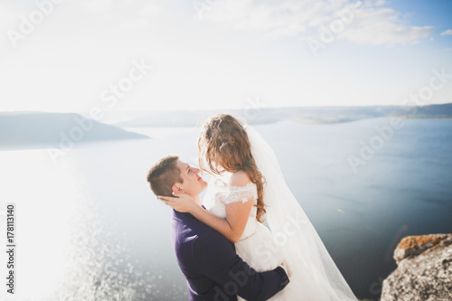 Wedding couple kissing and hugging on rocks near blue sea © olegparylyak