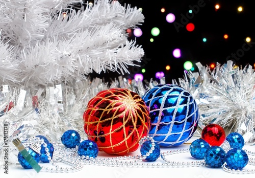 White christmas tree standing in the sparkling tinsel with christmas decorations on dark background with blurred lights