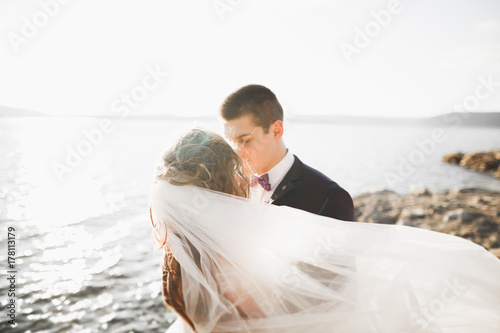 Wedding couple kissing and hugging on rocks near blue sea © olegparylyak