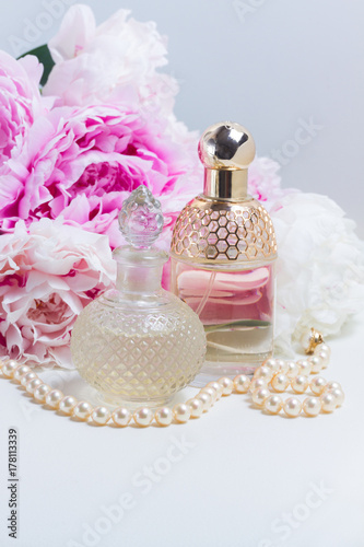 Peony essence in glass vials and fresh peony flowers on white leather background