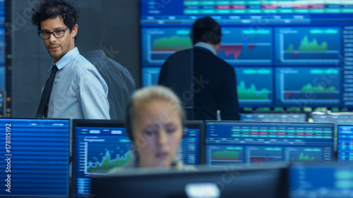 Stock Trader Goes Out of Office and Inspects Office. Busy Office with Multi-Ethnic Team of Brokers, Dealers. Displays Show Numbers and Infographics.