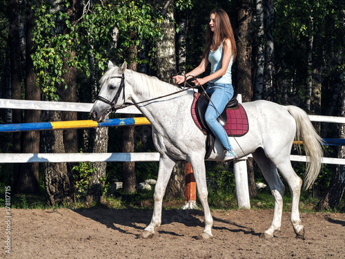 A beautiful girl is riding a white horse. Summer sunny day.