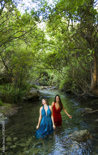 Two beautiful women on the bank of a mountain river with evening dresses