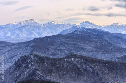 Beautiful scenic winter mountain landscape of Lagonaki mountain region with snowy peaks and forest valley. Bolshoy Tkhach mountain peak on background. Caucasus, Russia