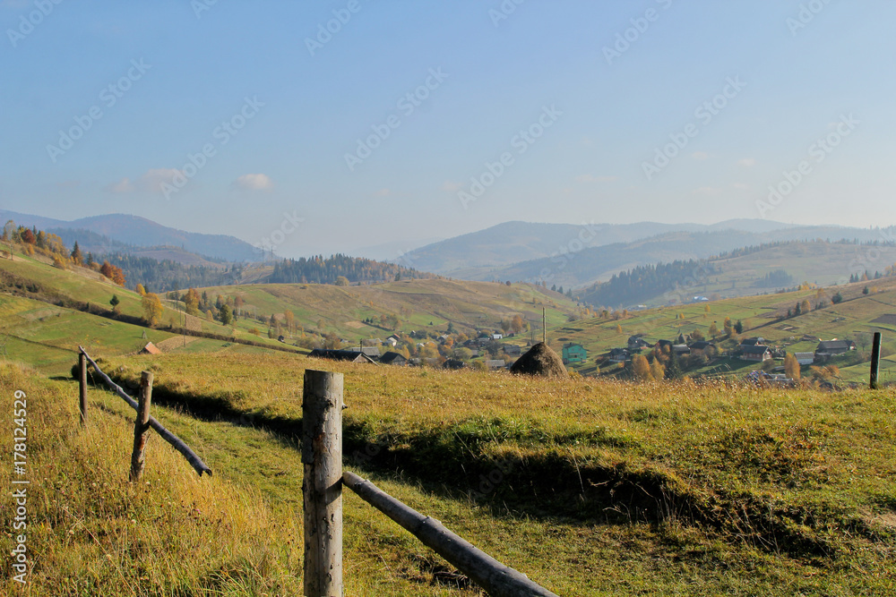 Landscape of mountain autumn village. Hill with green, orange and yellow colorful trees. Countryside in the fall time. Background of the Carpathian mountains in the Ukraine.