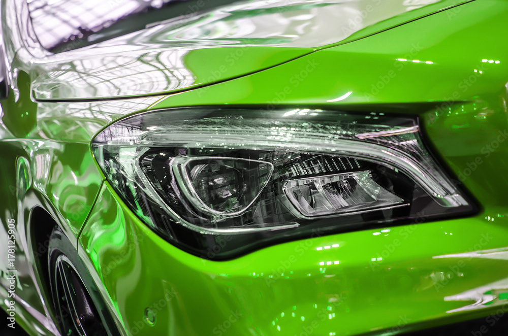 The headlamp of a green sports car of aggressive form with a part of the hood and black wheel, bumper and partronik