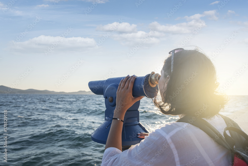 Obraz premium Young woman looks in a telescope or binoculars by the sea.